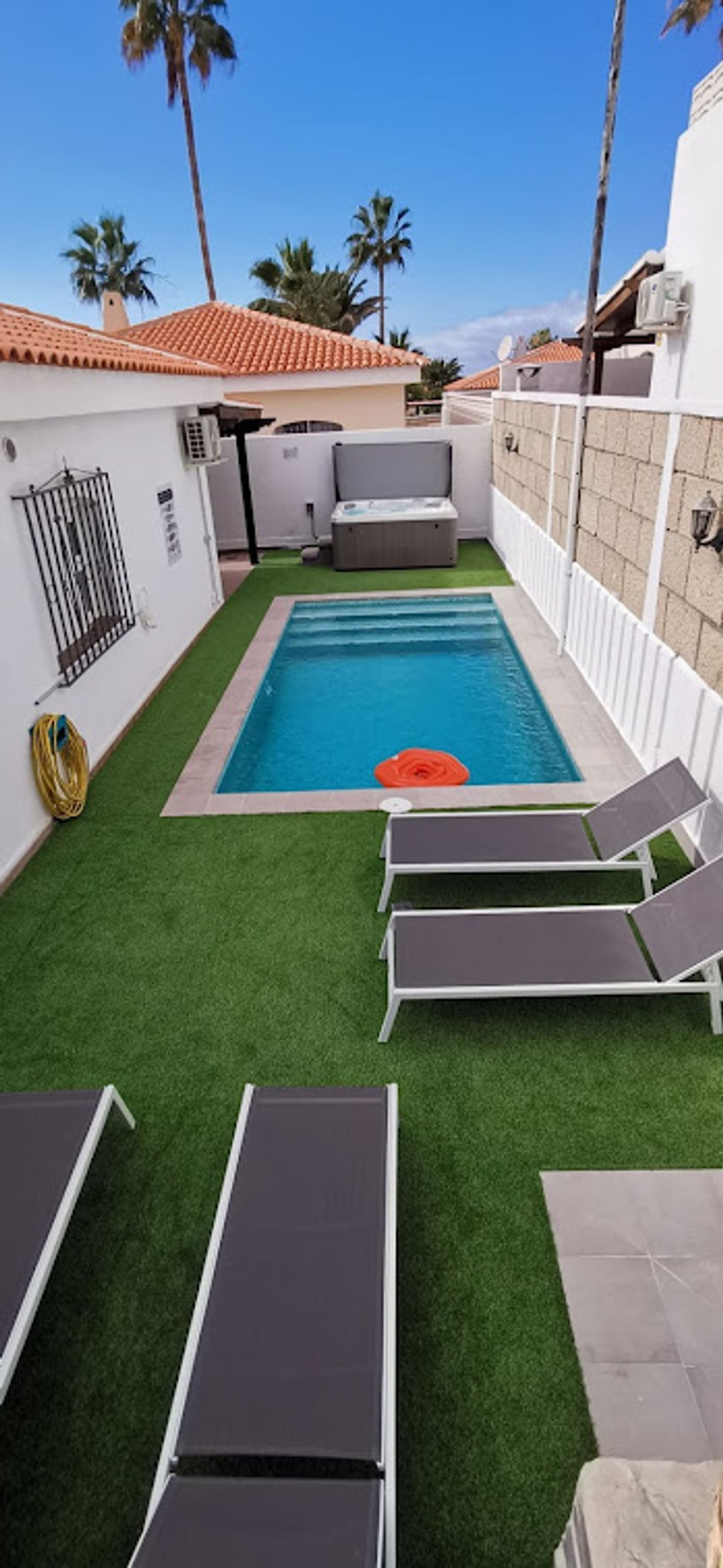 A swimming pool with artificial grass, lounge chairs, and palm trees in the background.