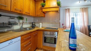 A kitchen with wooden cabinets, a dishwasher, an oven, a sink, and a countertop with a bottle of wine and glasses. - Villa Rosa in Callao Salvaje (Adeje)