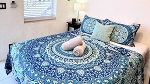 Een slaapkamer met een bedovertrek met patroon, een opgerolde handdoek en een hangende plant.