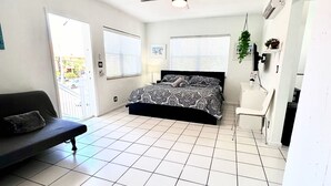 A bedroom with a bed, a desk, a chair, a ceiling fan, and a window.