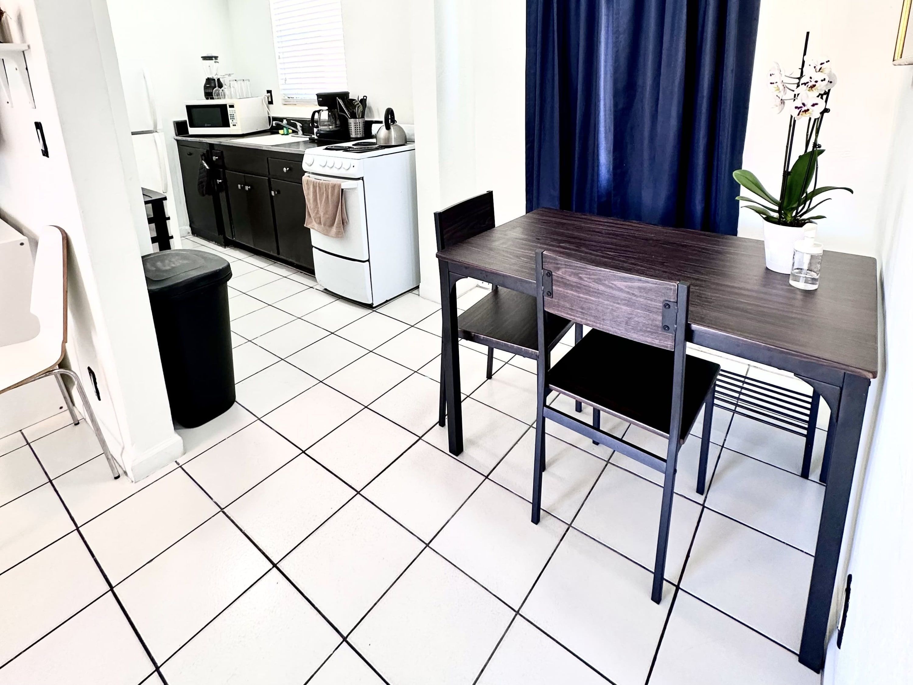 A compact kitchen with a white stove, black cabinets, and a blue curtain.