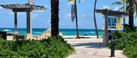 A beach pathway with palm trees, a gazebo, and a lifeguard tower.