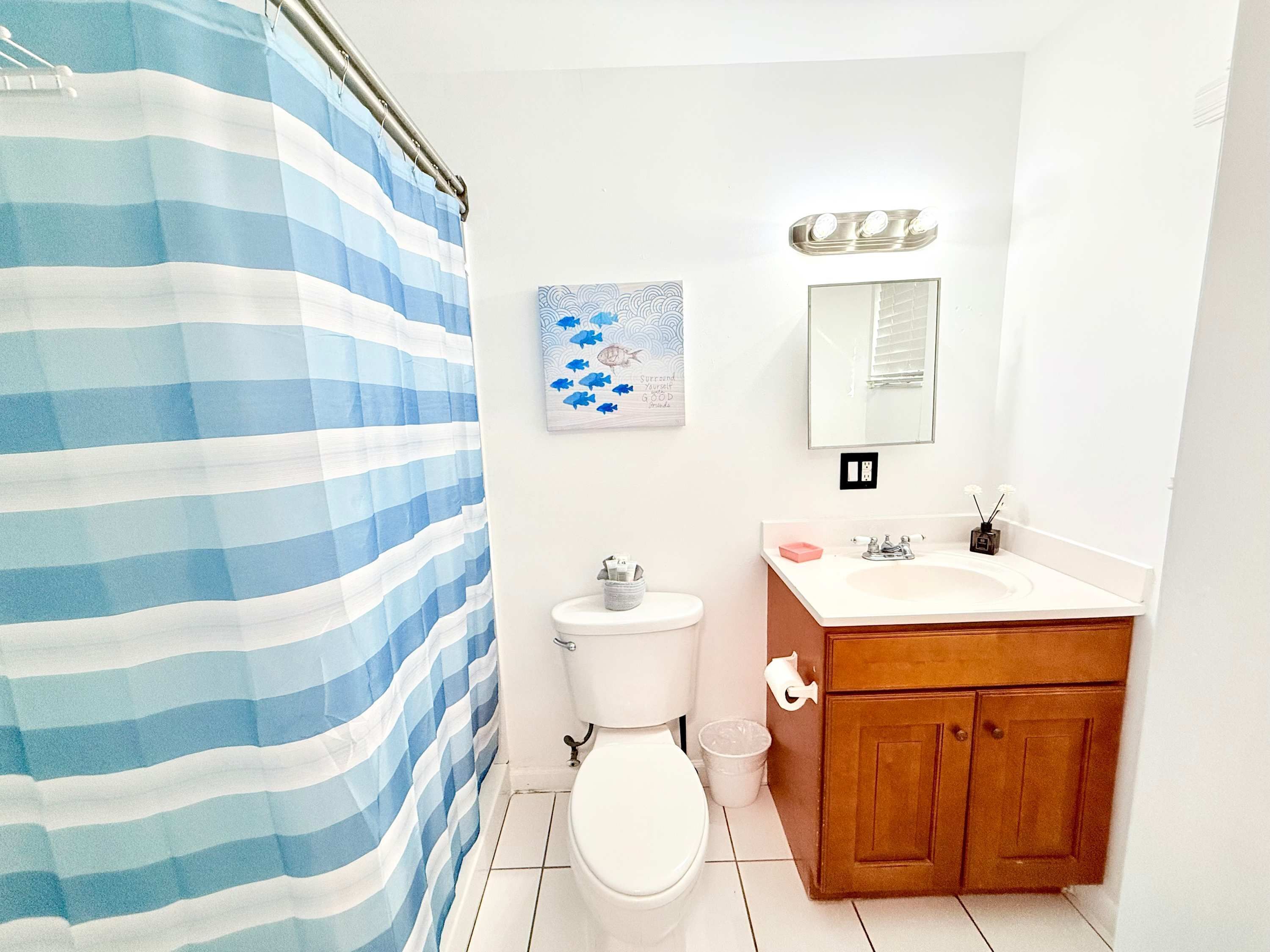 A bathroom with a striped shower curtain, a toilet, a sink with a mirror above it, and a small decorative item on the sink.