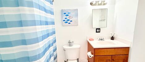 A bathroom with a striped shower curtain, a toilet, a sink with a mirror above it, and a small decorative item on the sink.