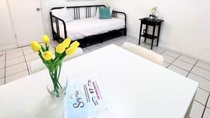 Hotellihuone, jossa on sänky, pieni pöytä, jossa on maljakko täynnä keltaisia kukkia, ja kaksi taulua seinällä.