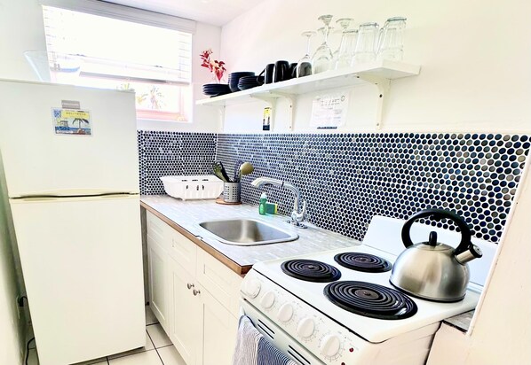Una cocina compacta con un refrigerador blanco, una estufa con cuatro hornillas, un lavamanos y un salpicadero de azulejos.