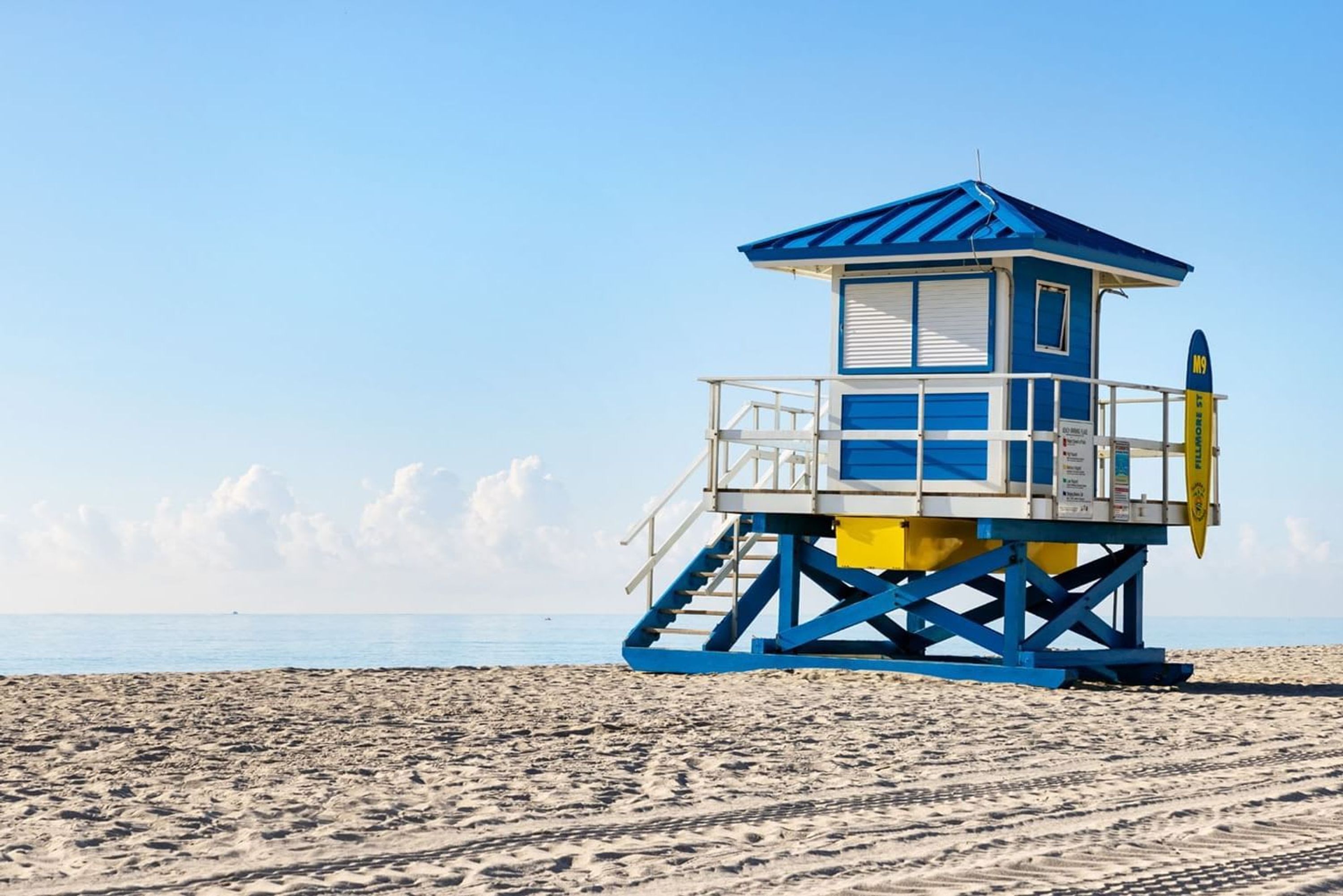 Een strandwachttoren met een blauw-wit kleurenschema, gelegen op een zandstrand met de oceaan op de achtergrond.