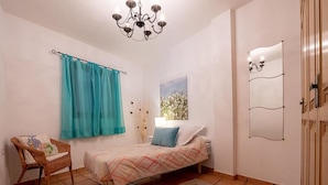 A bedroom with a bed, a chair, a chandelier, a mirror, and a window with curtains. - Apartamento Vulcano in Adeje (Adeje)