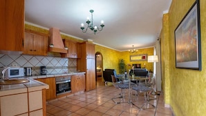 A kitchen with wooden cabinets, a microwave, and a dining area with a glass table and chairs. - Apartamento Vulcano in Adeje (Adeje)