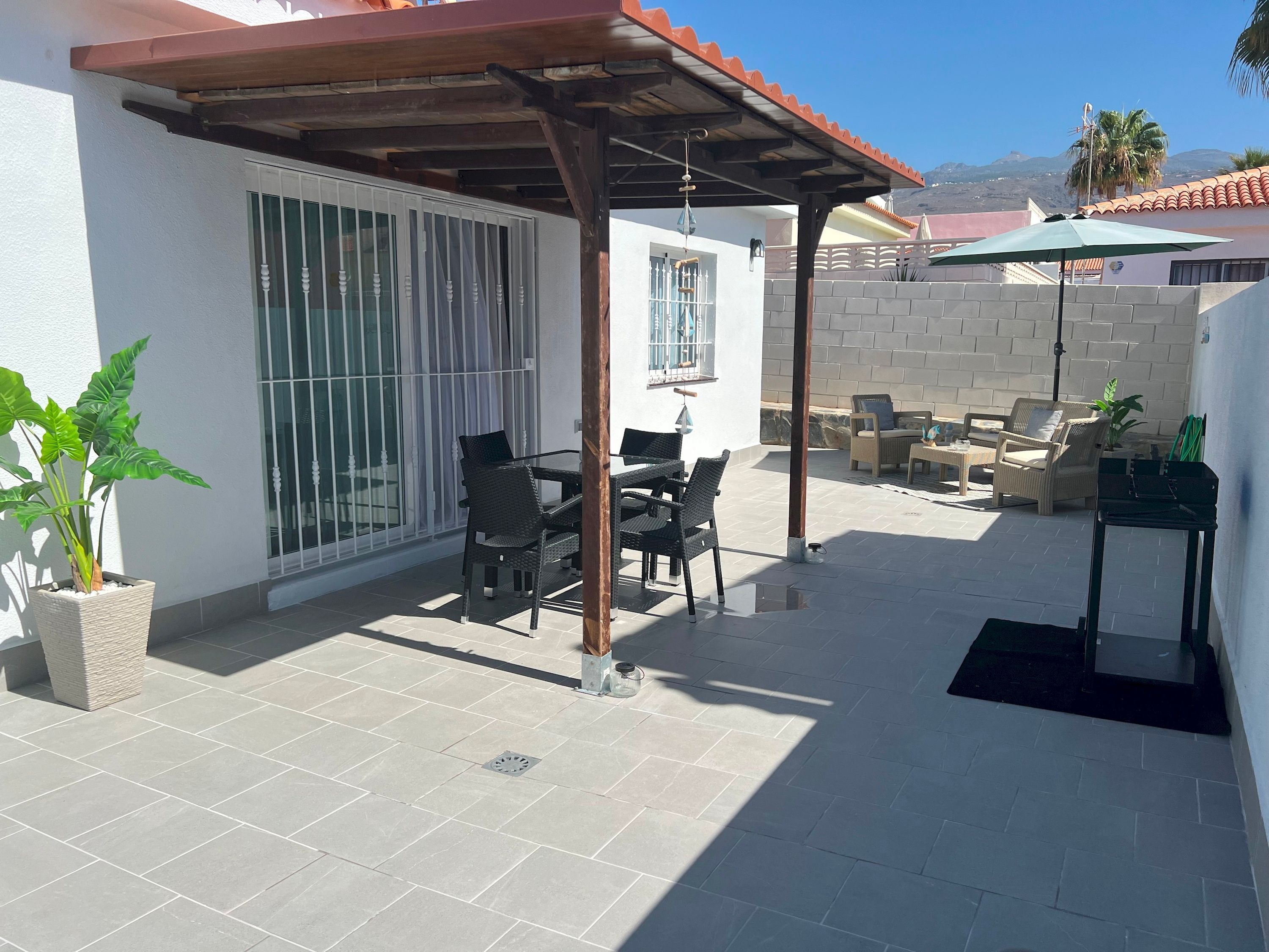 A patio with a covered seating area, a potted plant, and a view of the surrounding neighborhood.