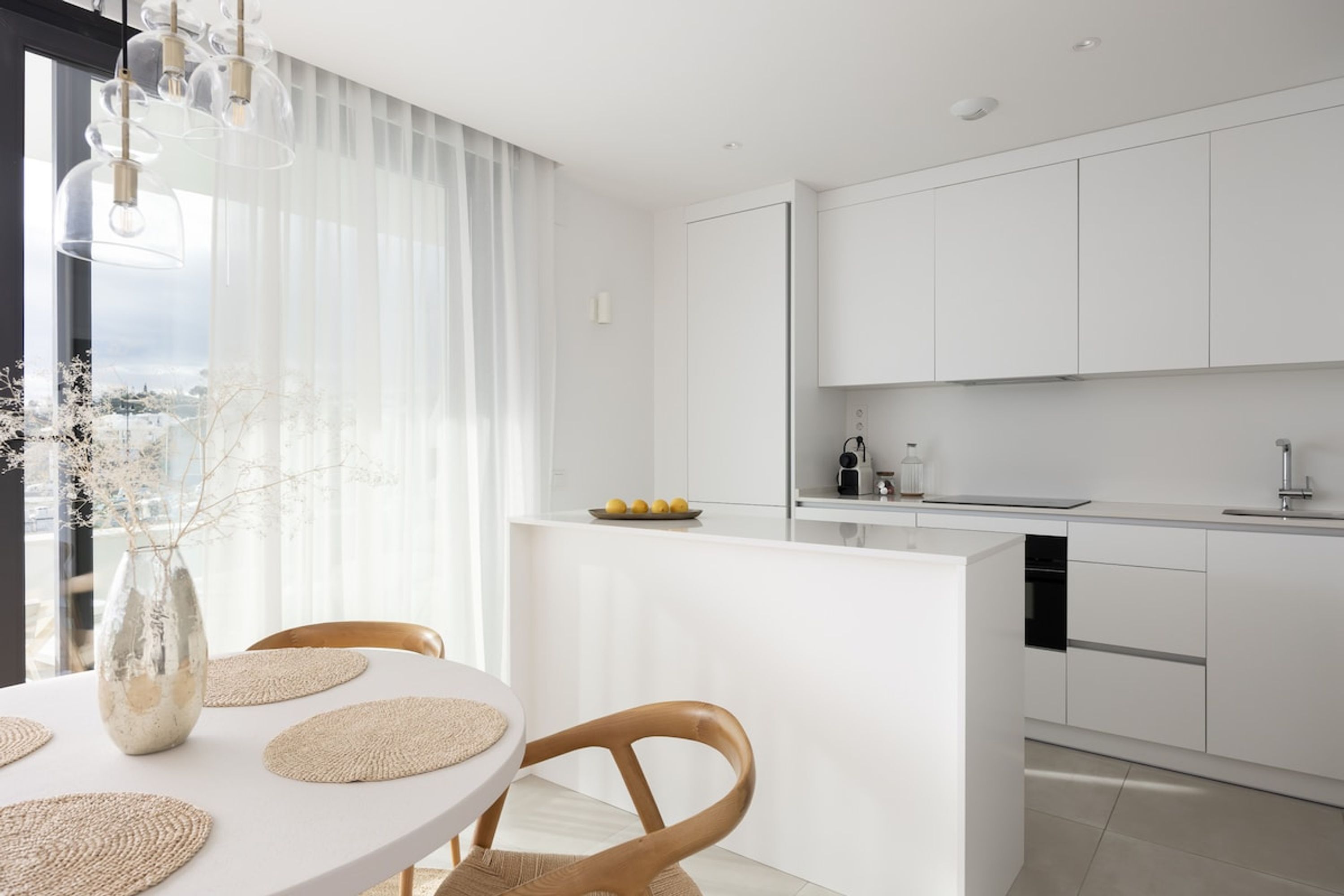 Una cocina moderna con armarios blancos, una isla central y una zona de comedor con una mesa redonda y sillas.