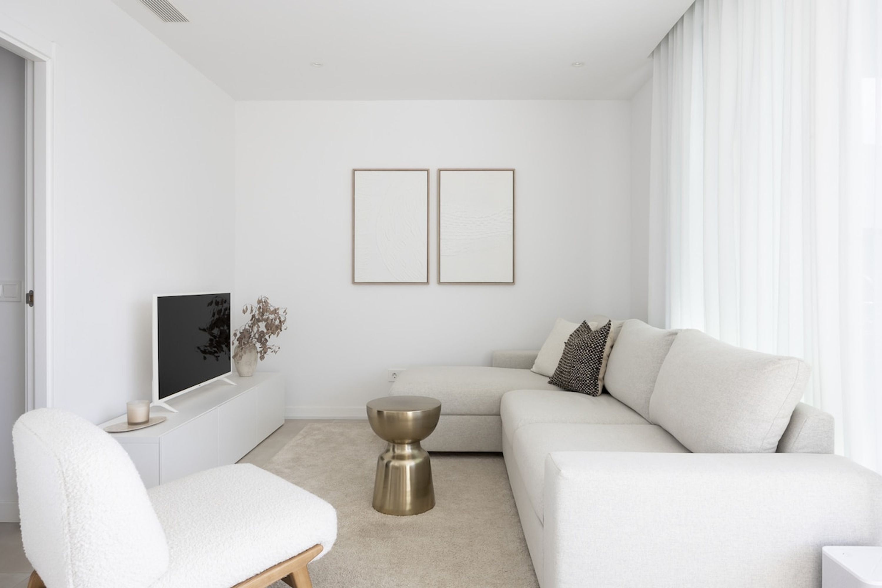 Ett modernt vardagsrum med en vit soffa, en vit fåtölj, ett litet runt bord och en platt-TV placerad på en vit TV-bänk.