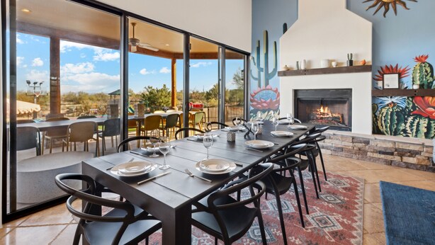 A dining area with a long table set for six, a fireplace, and a mural of cacti.
