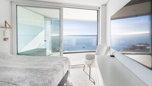 Une chambre moderne avec un grand lit, une porte vitrée donnant sur un balcon et une vue sur l’océan.