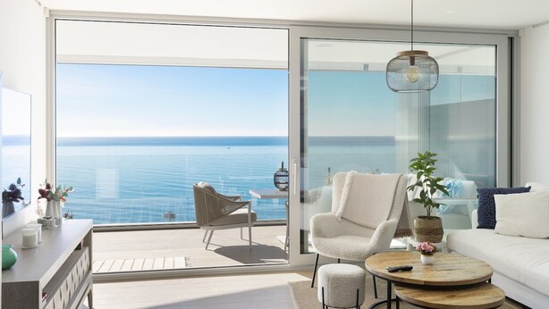Un salon moderne doté d’une grande porte-fenêtre coulissante donnant sur un balcon avec vue sur la mer.