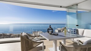 Un balcon avec vue sur la mer, une table avec une bouteille et des verres, et des meubles en osier.