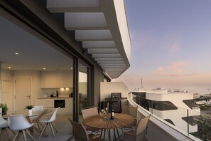 A modern balcony with a glass table and chairs, overlooking a cityscape.