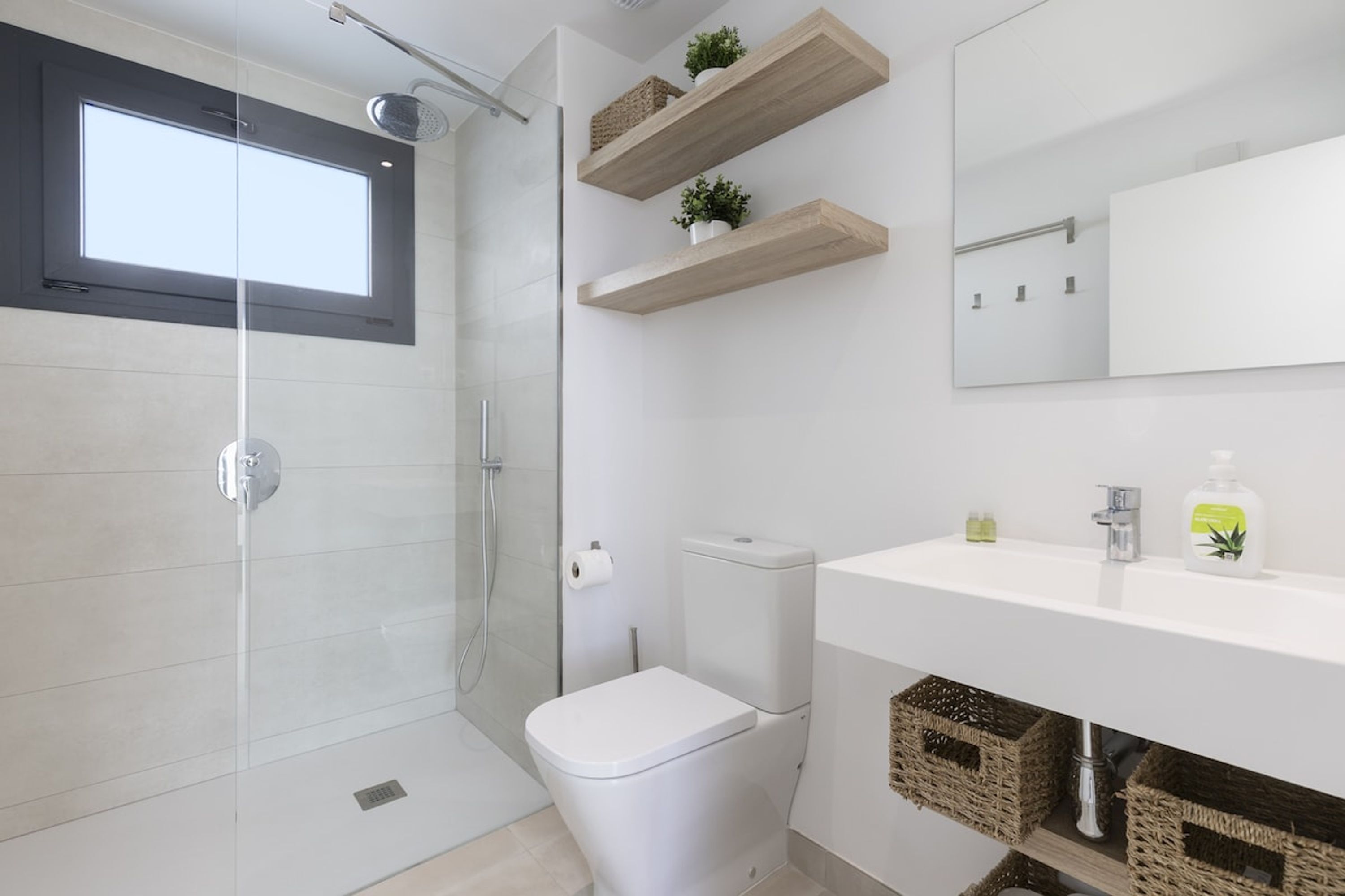 A modern bathroom with a glass shower enclosure, a toilet, and a vanity with storage baskets.