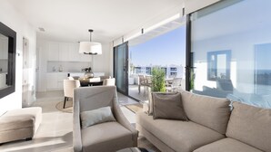 Een moderne woonkamer met een bank, een eethoek en grote ramen met uitzicht over de stad.