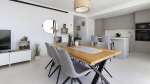 Une cuisine moderne avec des meubles blancs, un îlot central et un coin repas comprenant une table en bois et des chaises grises.