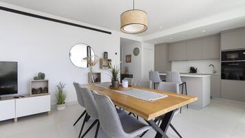 Une cuisine moderne avec des meubles blancs, un îlot central et un coin repas comprenant une table en bois et des chaises grises.
