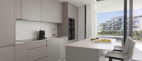 A modern kitchen with a central island, grey cabinetry, and a view of a residential area through large windows.