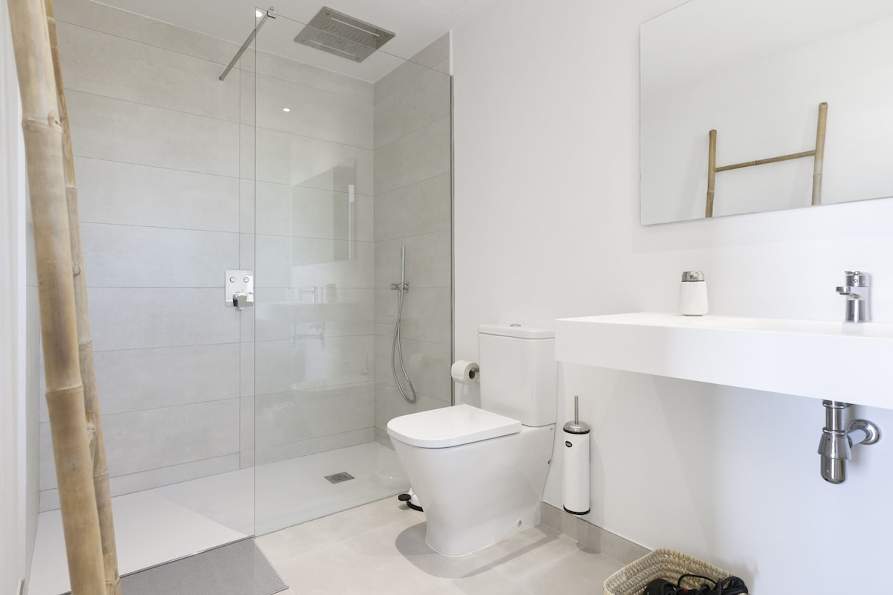 A modern bathroom with a glass shower enclosure, a white toilet, and a sink with a mirror above.