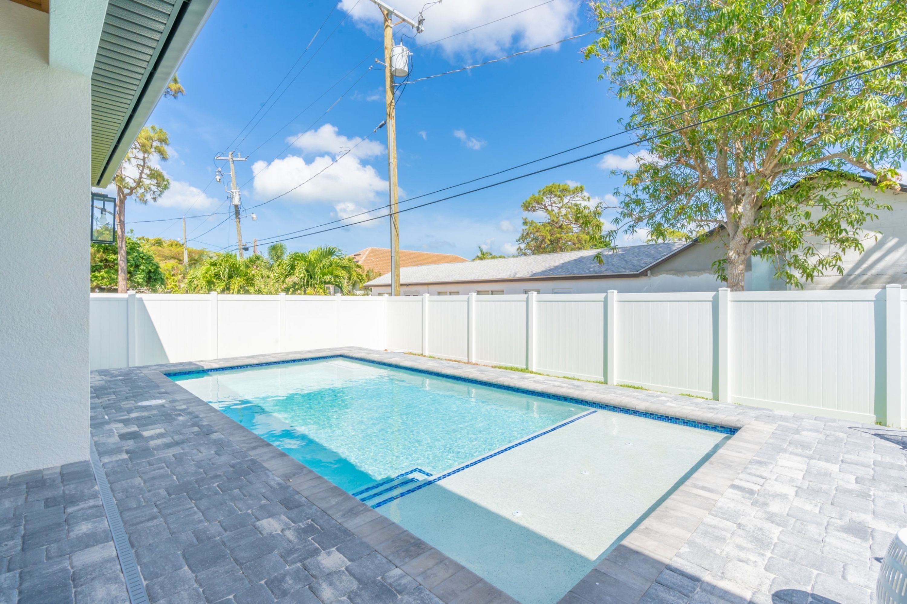 Une piscine rectangulaire à l’eau d’un bleu limpide, entourée d’une clôture blanche et d’une terrasse dallée.