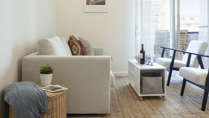 A living room with a sofa, a side table with a wine bottle, a chair, a plant, and a framed picture on the wall. - Beachfront Apartment With Seaview Terrace (Fuengirola)