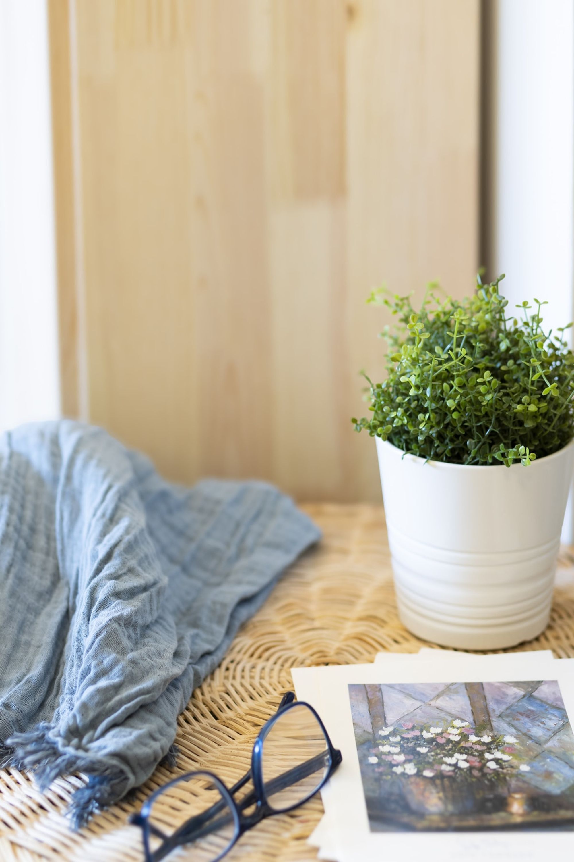 A wicker table with a potted plant, a pair of glasses, and a framed photograph.