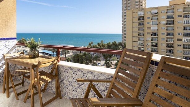 A balcony with wooden furniture, a view of the sea, and a tall building in the background. - Beachfront Apartment With Seaview Terrace (Fuengirola)