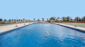 A rectangular swimming pool with a clear blue water surface, surrounded by a tiled deck and palm trees. - Beachfront Apartment With Seaview Terrace (Fuengirola)