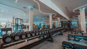 Een fitnessruimte met gewichthefapparatuur, banken en een spiegelwand.