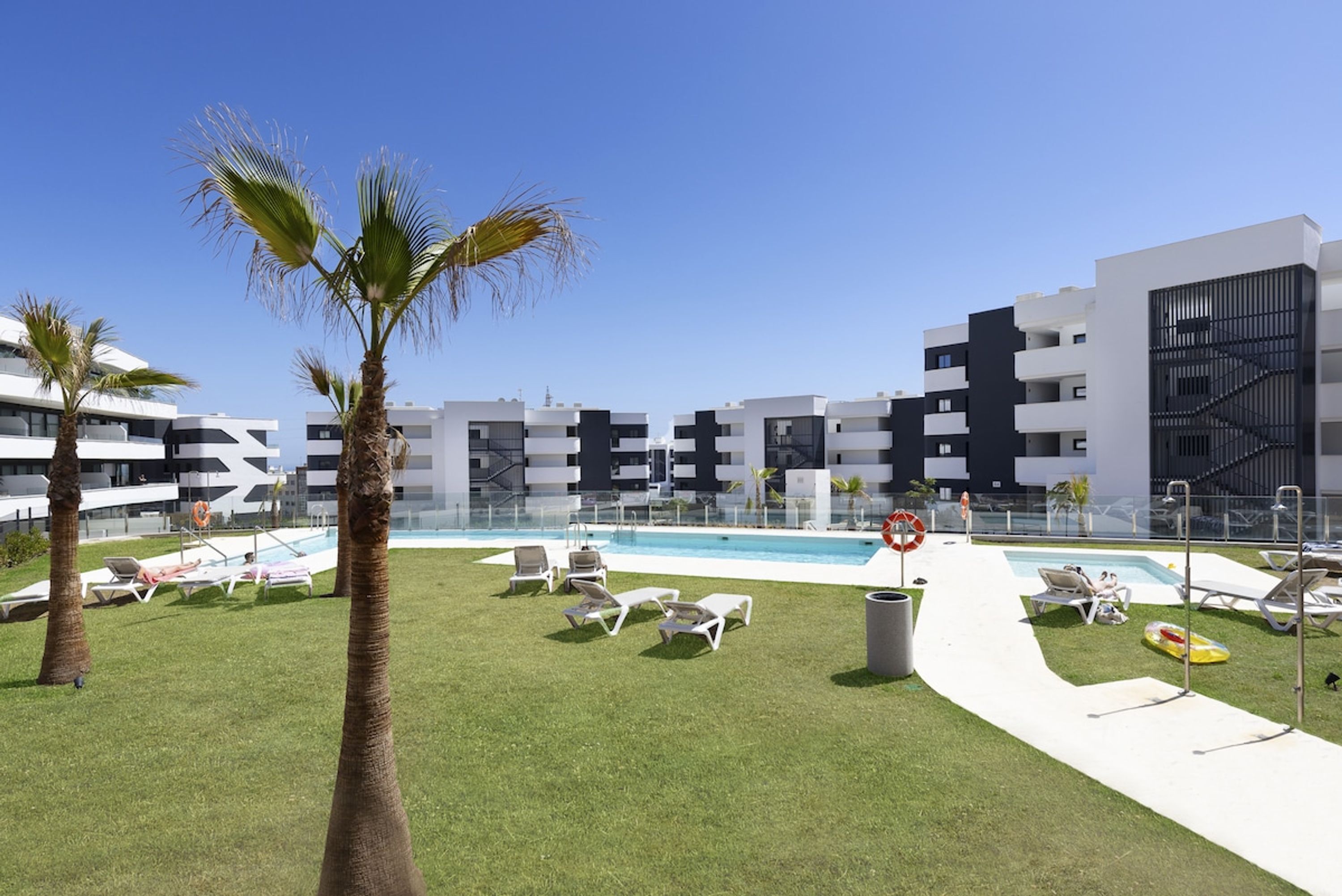 A modern hotel with a swimming pool, palm trees, and lounge chairs.