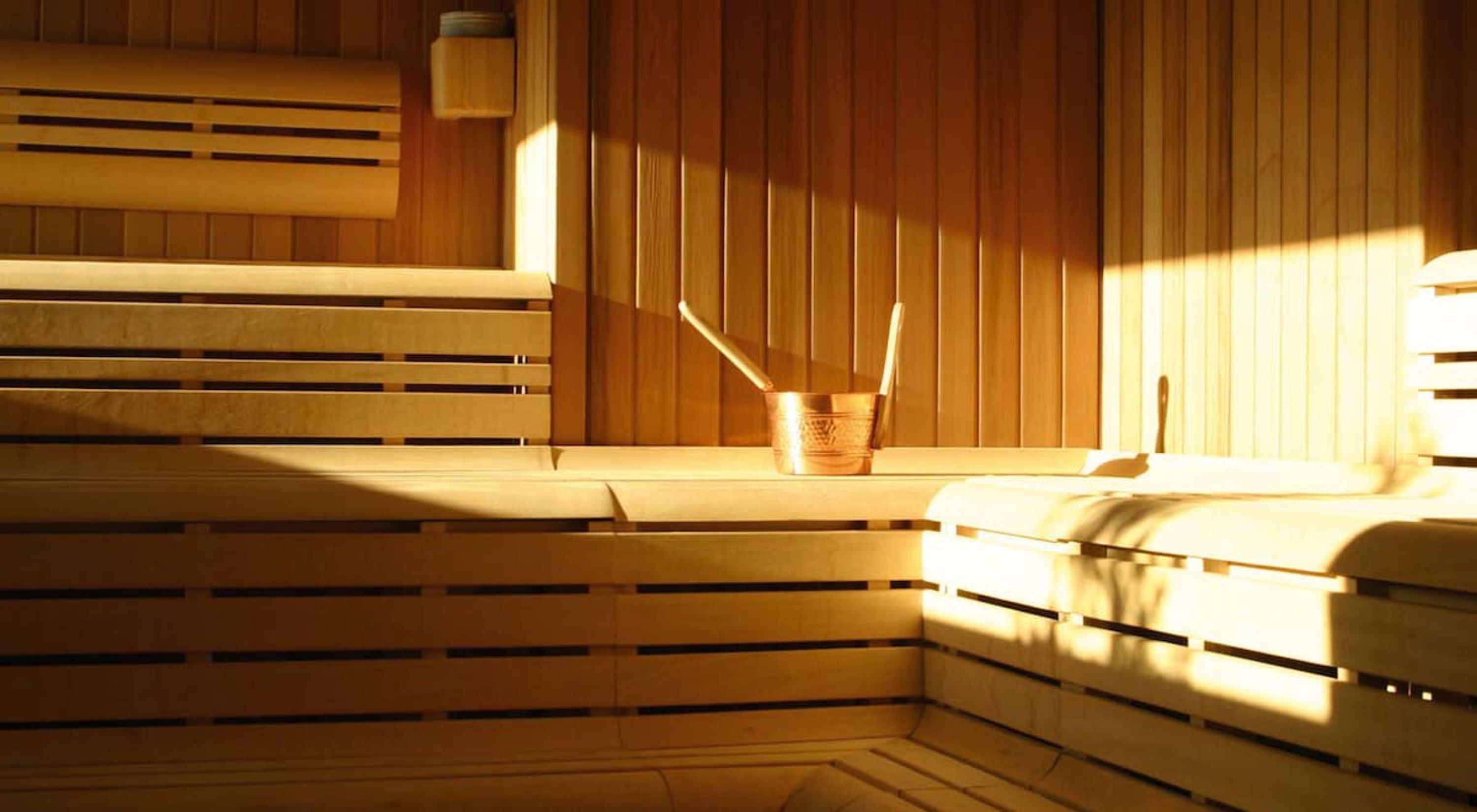 Un sauna avec des bancs en bois et un seau en cuivre.