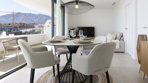 Een moderne eetruimte met een ronde tafel, stoelen en een groot raam met uitzicht op bergen en bouwactiviteiten.