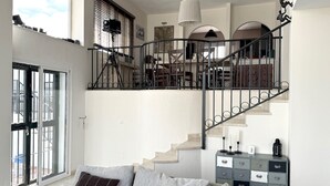 A spacious living area with a grey sofa, a staircase with a metal railing, and a view of the outdoors through large windows. - Casa Kodak - Las Lagunas de Mijas (Mijas)