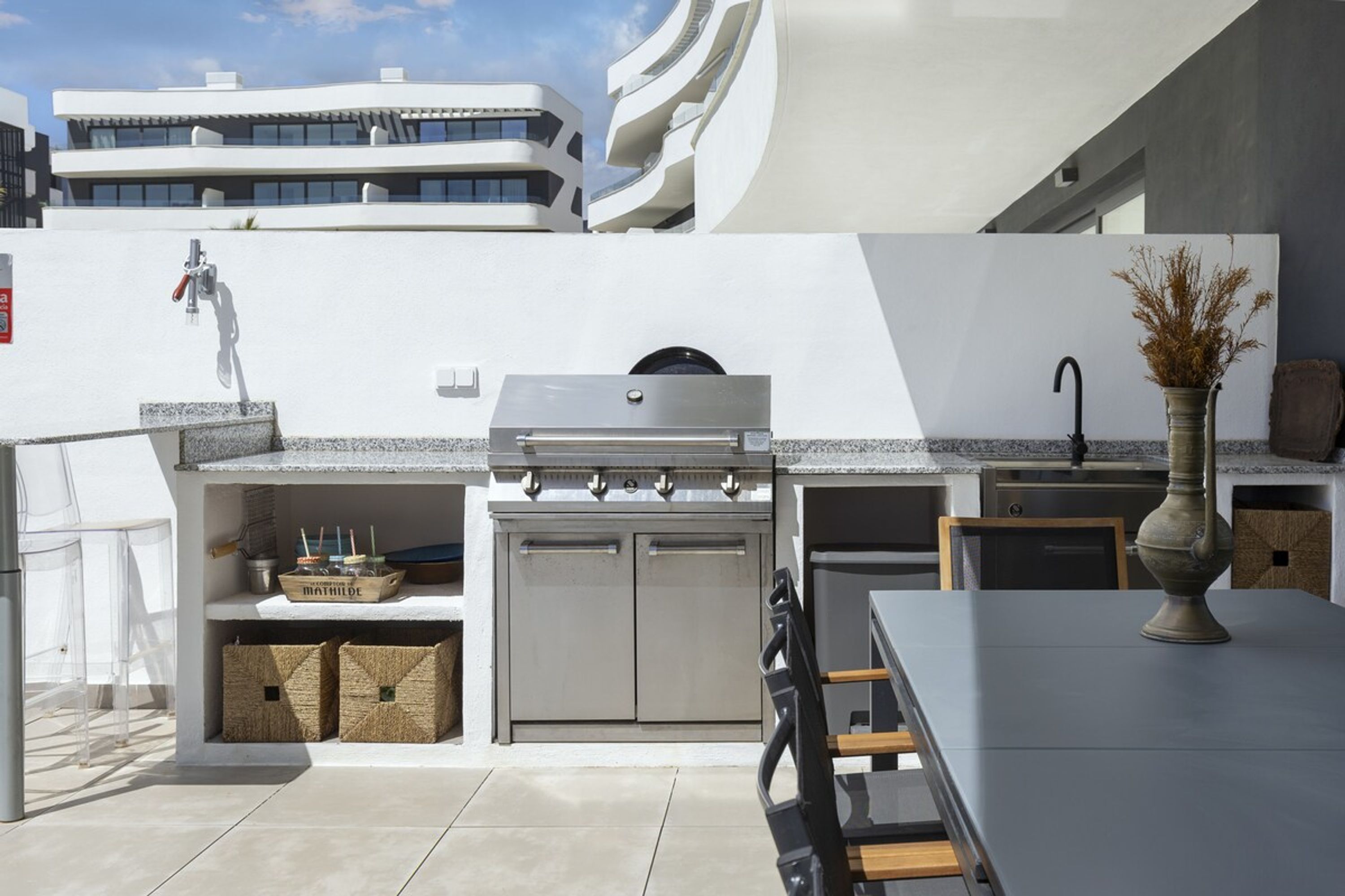 Une cuisine extérieure équipée d’un barbecue encastré, d’un évier et d’un espace repas avec une table et des chaises.