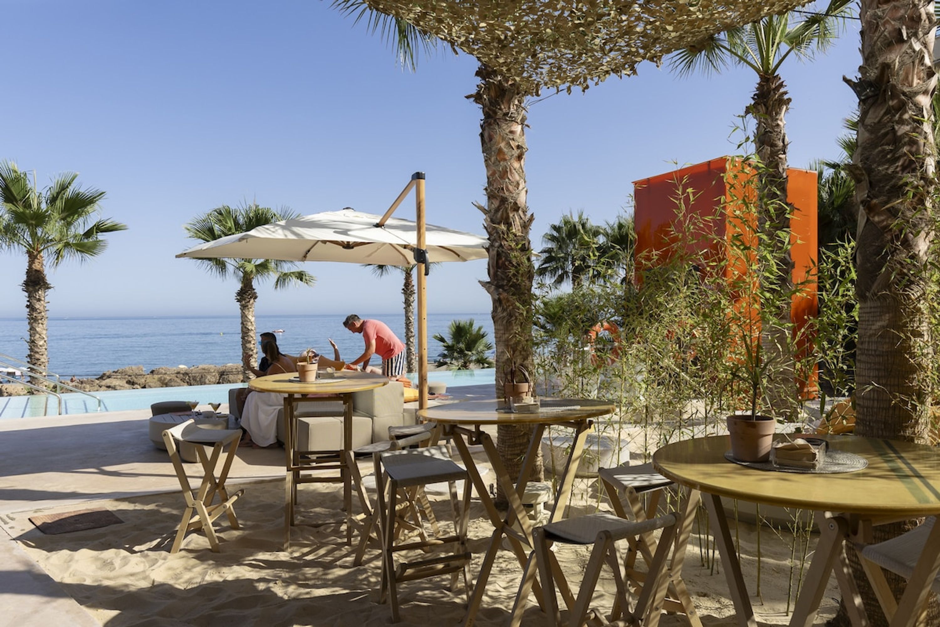 An outdoor seating area with tables and chairs, a pool, and palm trees.