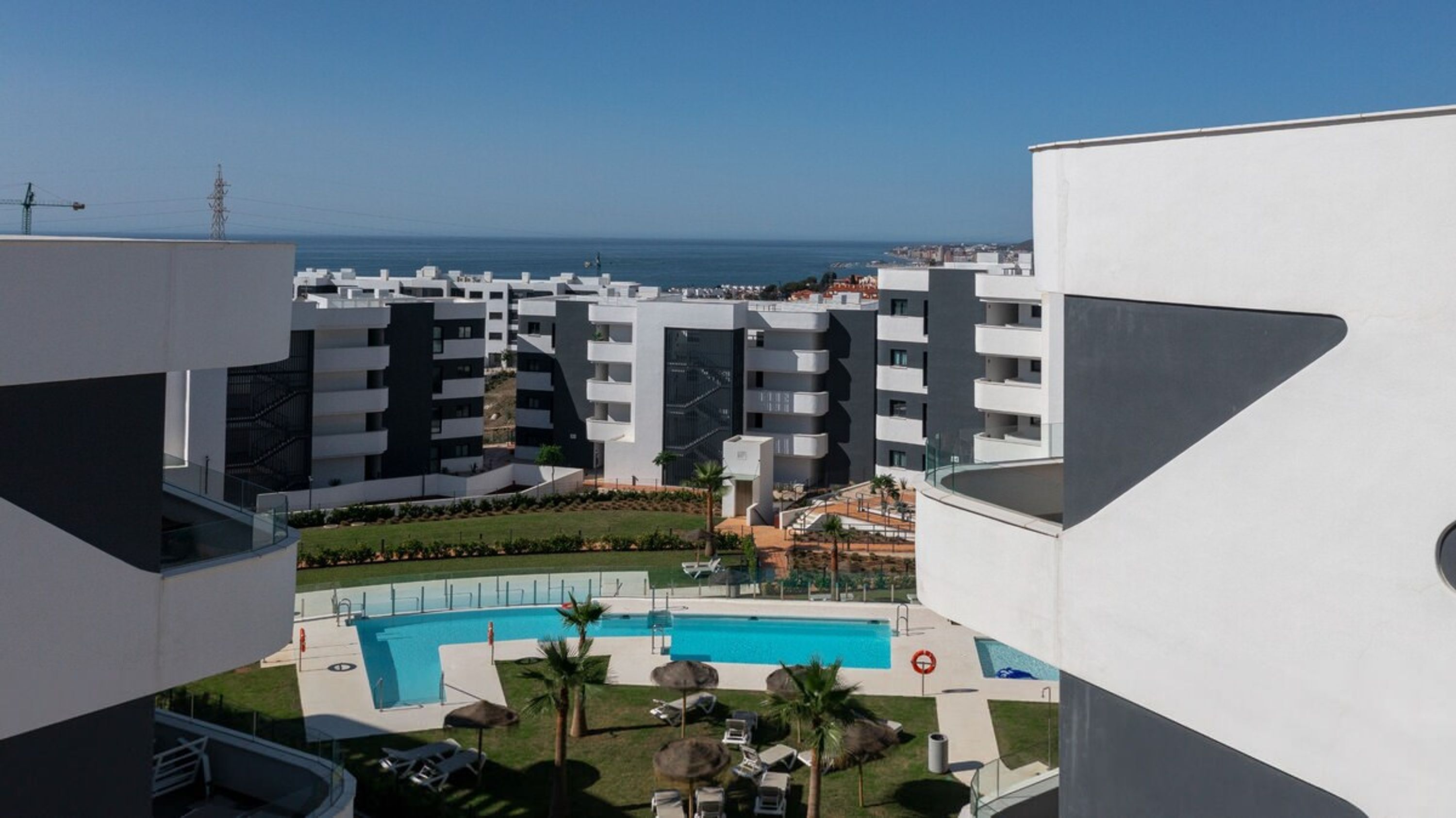 Et moderne lejlighedskompleks med swimmingpool, altaner og havudsigt.