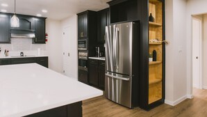 A modern kitchen with dark cabinetry, a stainless steel refrigerator, and a white countertop. - Misha: 6443 Redpine Road, Dallas (Dallas)