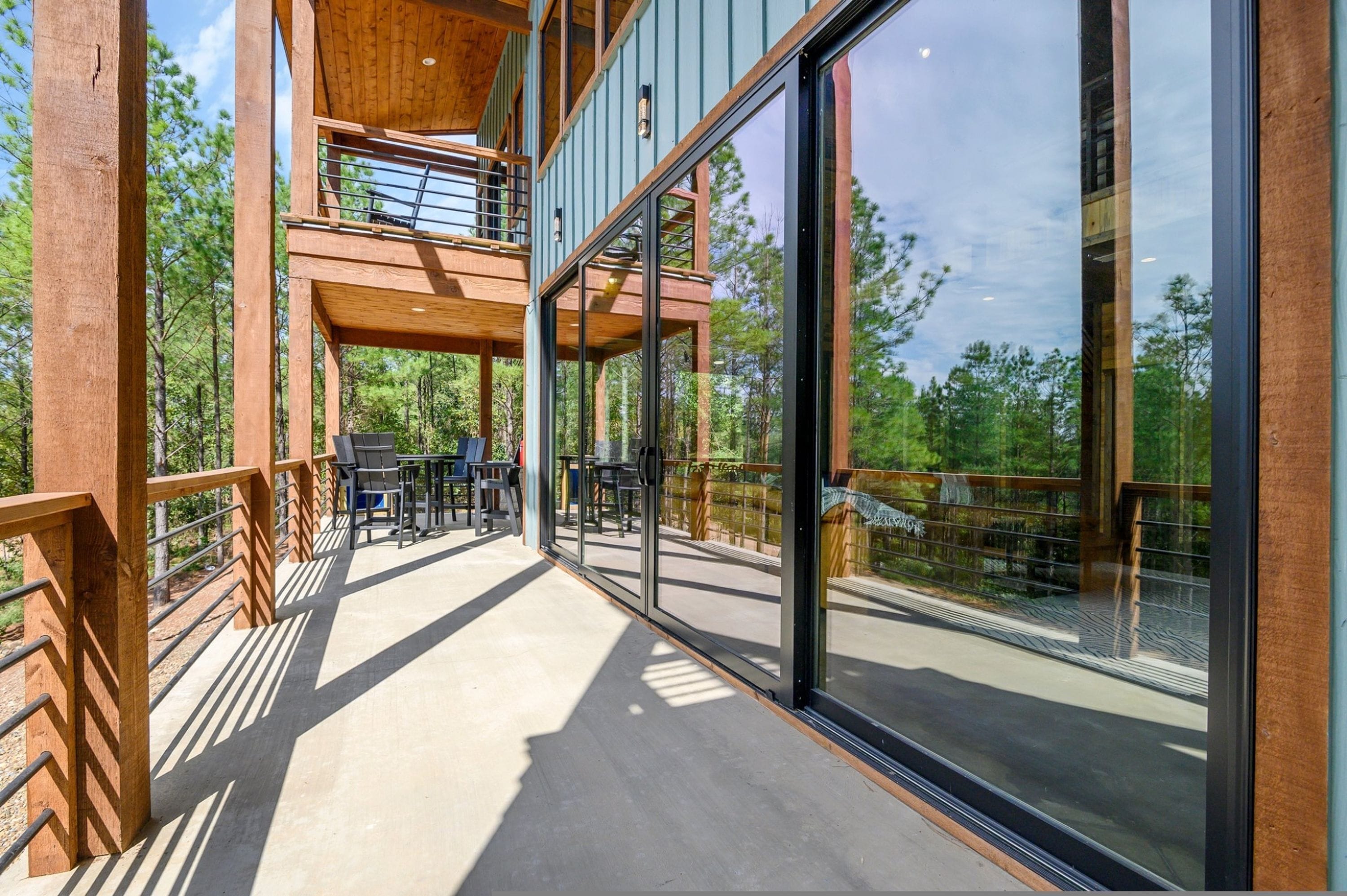 A multi-level wooden deck with glass railings, outdoor furniture, and a view of the surrounding forest.