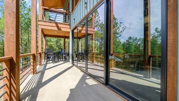 A multi-level wooden deck with glass railings, outdoor furniture, and a view of the surrounding forest.
