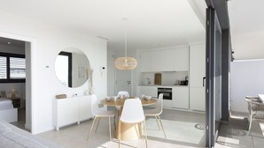 Una cocina moderna con armarios blancos, una mesa redonda de comedor con sillas blancas y una lámpara colgante.