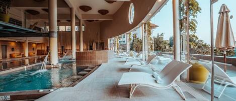 Un área de piscina con sillones reclinables, un elemento acuático y grandes ventanales.