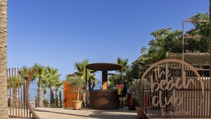 A beach club entrance with a palm tree-lined pathway and a sign reading "the beach club". - Luxury Apartment With Terrace in Higueron (Fuengirola)