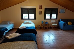 A cozy attic bedroom with two beds, a small desk, and a blue sofa. - Edificio Taratola (Ortigosa del Monte)