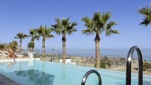 A swimming pool with clear blue water, surrounded by palm trees and a view of the ocean. - Exclusive 3-bedroom Apartment in Higueron (Fuengirola)