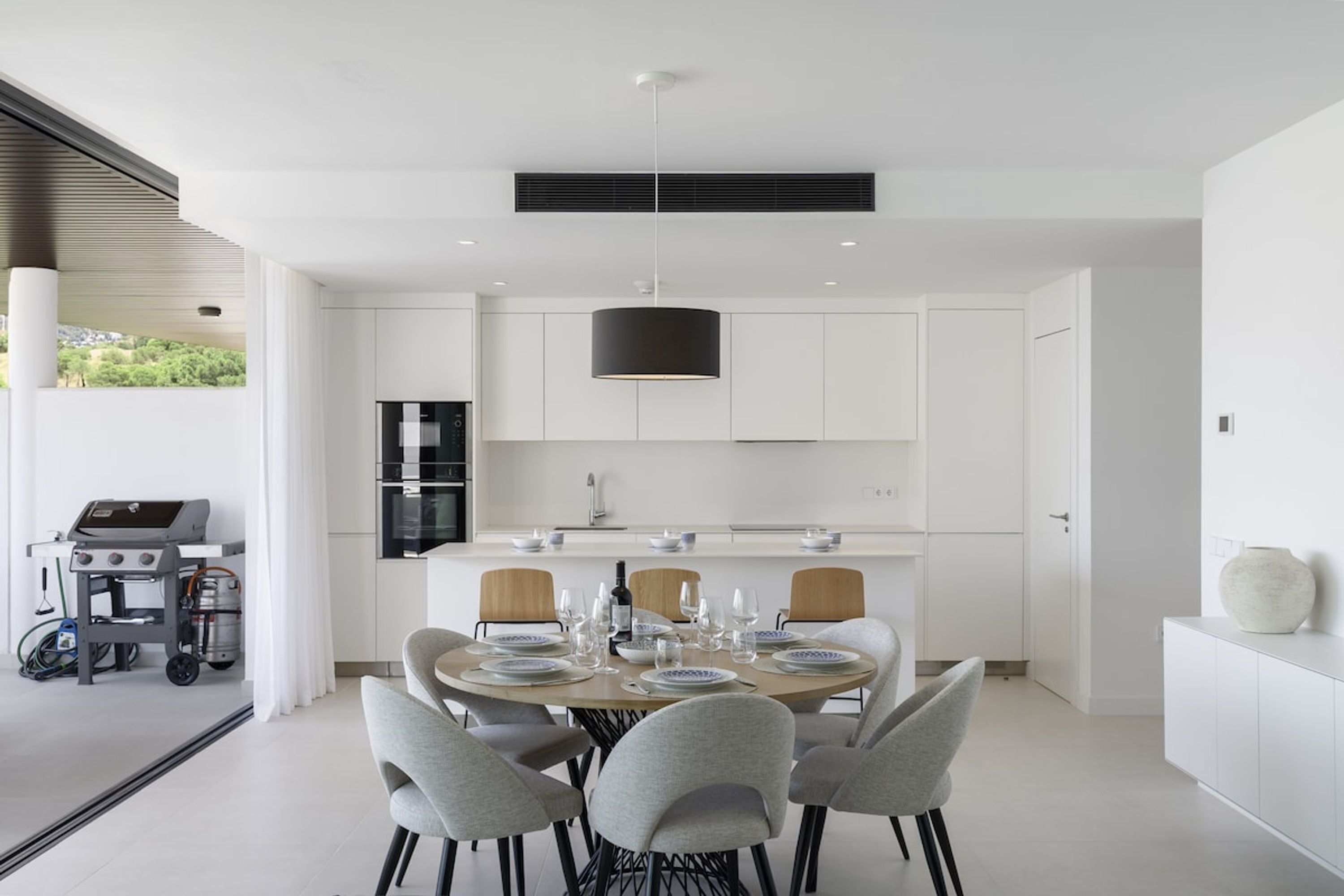 Una cocina moderna con armarios blancos, una isla central y un comedor con una mesa redonda y sillas.