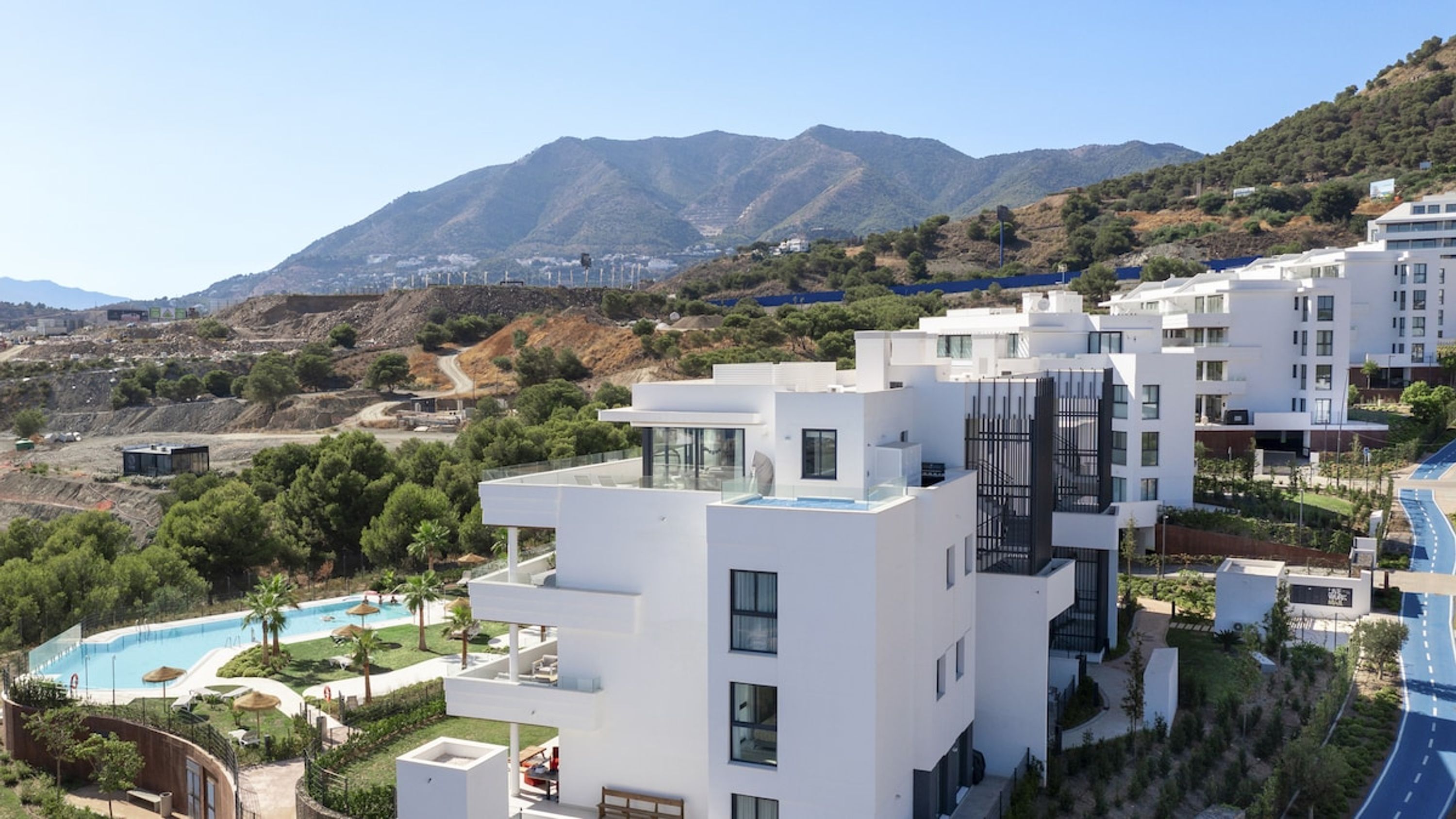 A modern hotel with a pool, surrounded by mountains and greenery.